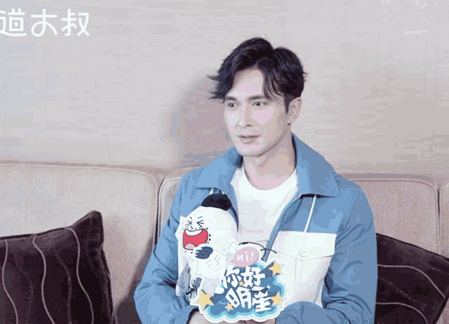 a man sitting on a couch with a sticker on his jacket that says hi