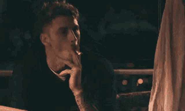 a man is smoking a cigarette while sitting in a car at night .