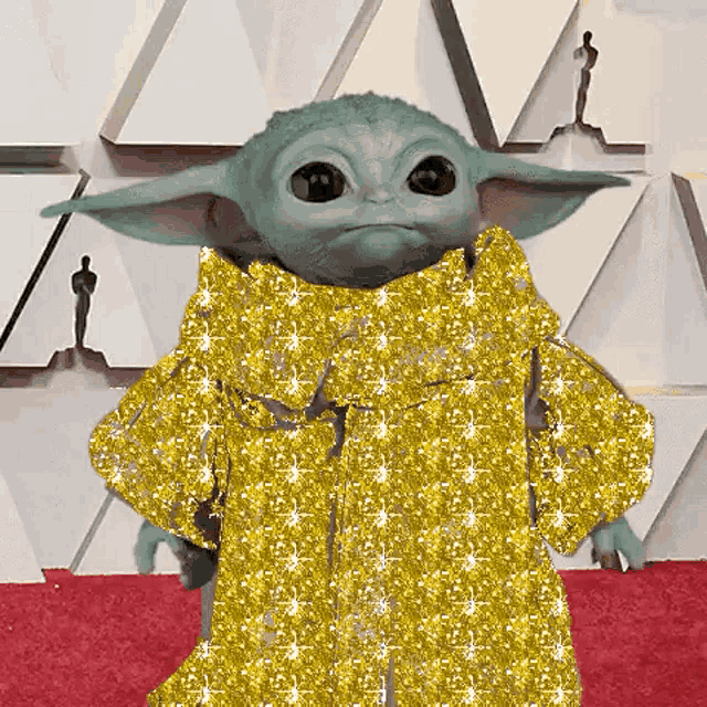 a baby yoda is wearing a gold dress and standing on a red carpet .