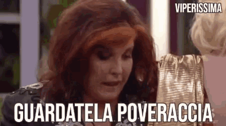 a woman with red hair is wearing a gold dress and a wig and is talking to another woman .