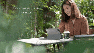 a woman sits at a table with a tablet and a cup of coffee and the words " i am allowed to take up space "