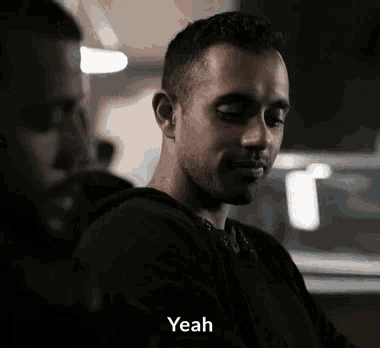 a man in a black hoodie is talking to another man in a dark room and saying yeah .