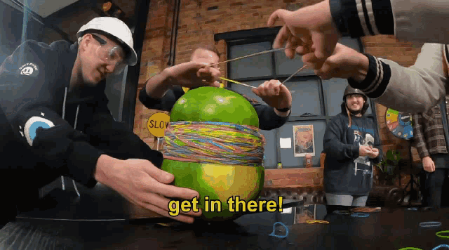a group of people are playing with a large green ball with rubber bands around it and the words " get in there " above them