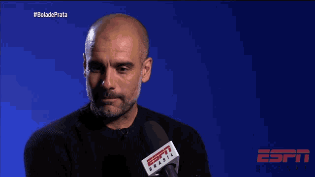 a bald man is talking into a microphone with the words " o futebol e emocao " on the screen