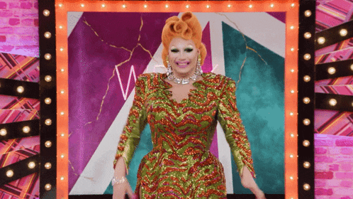 a drag queen in a green and red dress stands in front of a sign that has the letter w on it