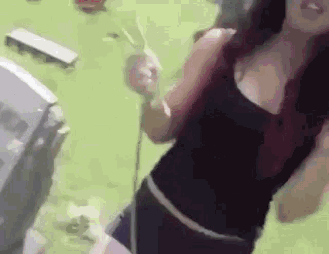 a woman in a black tank top is standing on a green carpet holding a microphone .