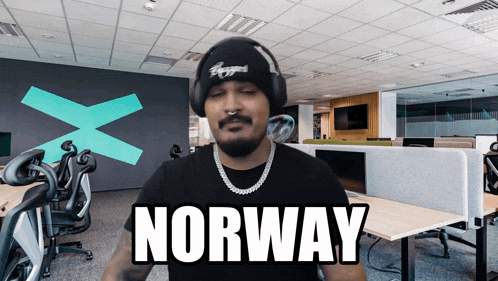 a man wearing headphones and a beanie says norway in an office