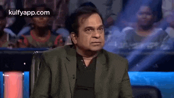 a man in a suit is sitting in front of a crowd and making a face .