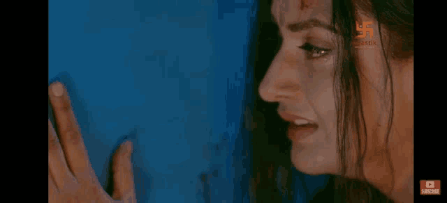 a close up of a woman 's face with blood on her forehead against a blue wall .