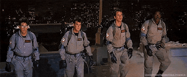 a group of men in ghostbusters uniforms are walking in front of a city at night .