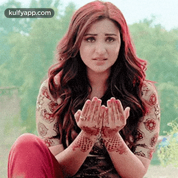 a woman with a henna tattoo on her hands is sitting on the ground with her hands folded in prayer .