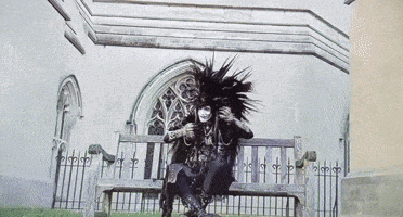 a person with a mohawk sits on a bench in front of a church