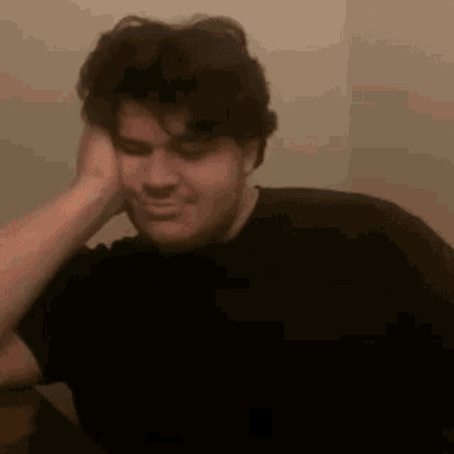 a man in a black shirt is holding his hand to his forehead and making a funny face .