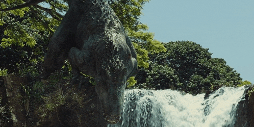 a statue of a dinosaur jumping over a waterfall with trees in the background