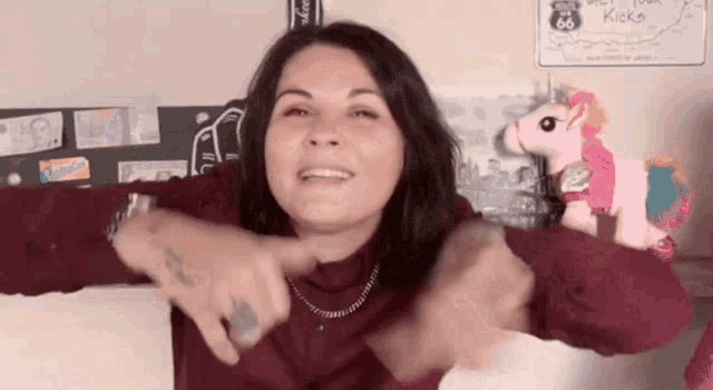 a woman in a red shirt is making a funny face in front of a pink stuffed unicorn .