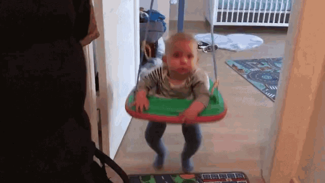 a baby is playing in a green and red swing in a hallway