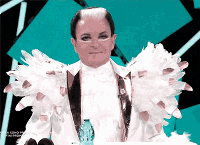 a man in a white suit with feathers on his shoulders is sitting at a table