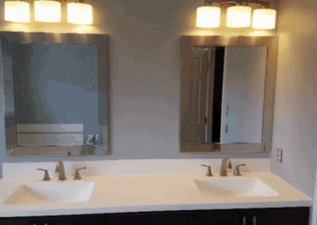 a bathroom with two sinks and two mirrors with lights on
