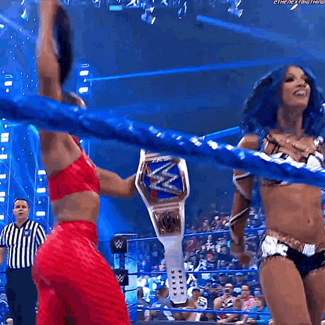 two women are standing in a wrestling ring holding a championship belt