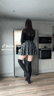 a woman in a plaid skirt is standing in front of a refrigerator in a kitchen