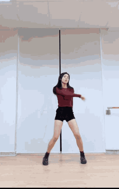 a woman in a red top and black shorts is dancing in a room .