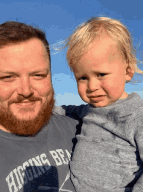 a man wearing a higgins beach shirt is holding a child