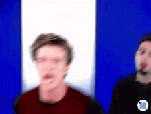 a blurry picture of two men standing next to each other in front of a blue and white wall .