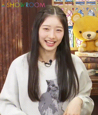 a woman wearing a white sweater with a cat on it is smiling in front of a showroom sign