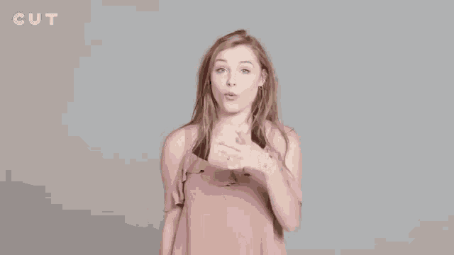 a woman in a pink top is standing in front of a gray background with the word cut on it .