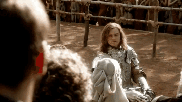 a woman in armor is sitting on the ground in front of a crowd of people