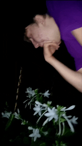 a person in a purple shirt is standing next to a flower