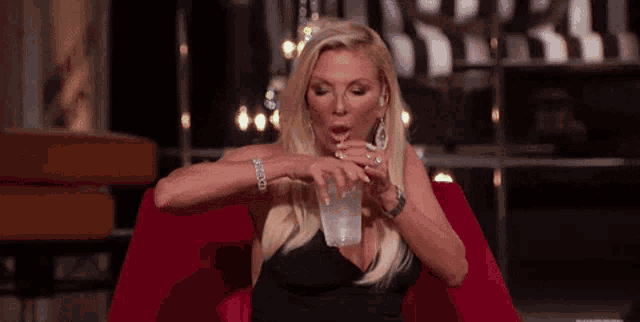 a woman in a black dress is sitting on a red couch drinking from a cup .