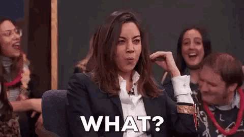 a woman in a suit is sitting in front of a group of people and saying what .