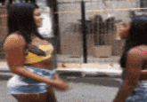 two women in shorts are standing next to each other on the street .