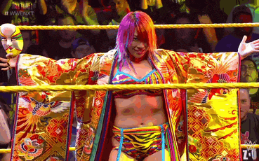 a woman in a kimono is standing in a wrestling ring with her arms outstretched in front of a crowd .
