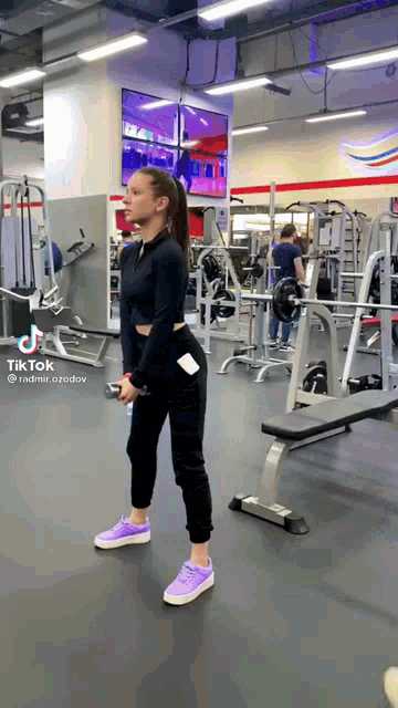 a woman is standing in a gym with a dumbbell in her hand .