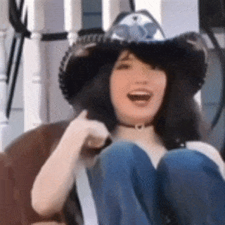a woman wearing a cowboy hat and choker is sitting on a couch .
