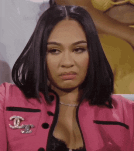 a woman is wearing a pink jacket with a chanel brooch on the front .