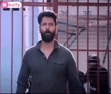 a man with a beard is standing in front of a fence in a prison cell .