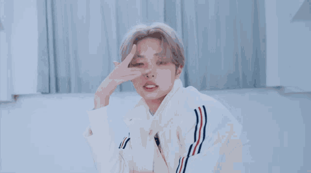 a young man wearing a white jacket with red white and blue stripes on the sleeves is making a peace sign