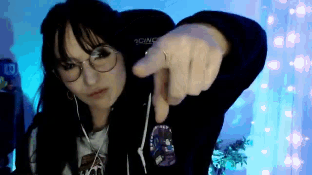 a woman wearing glasses and headphones is pointing at the camera with her finger .