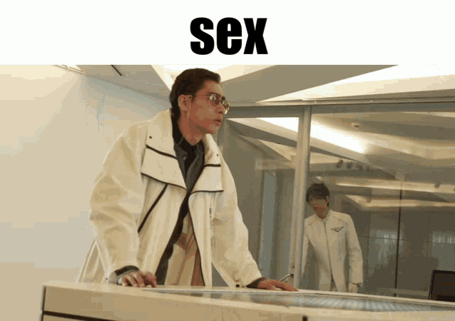 a man in a white coat is standing in front of a glass wall with the word sex written above him