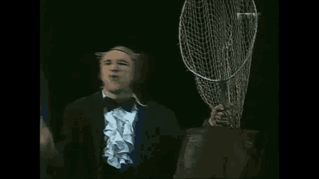 a man in a tuxedo is holding a fishing net in his hand .