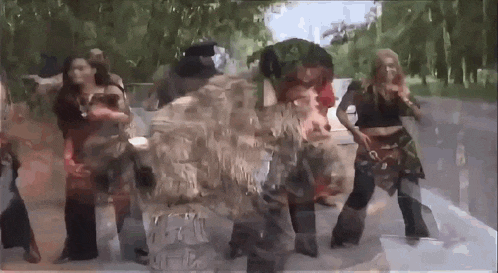 a group of people are dancing on a street in front of trees