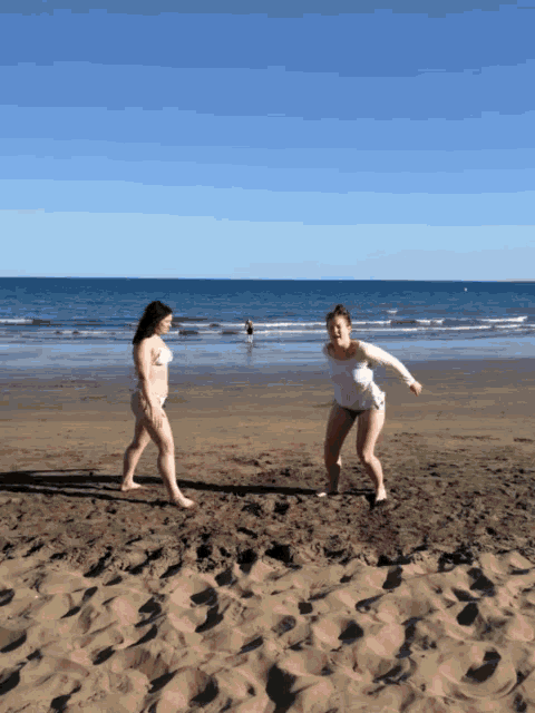 two women in bikinis are playing on a sandy beach near the ocean