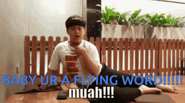 a boy is sitting on a table with the words baby ur a flying word muah