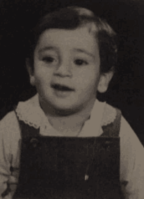 a black and white photo of a young boy wearing overalls and a white shirt