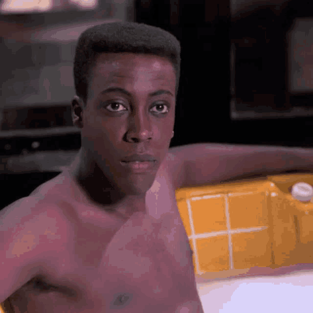 a shirtless man is leaning on a yellow tiled wall