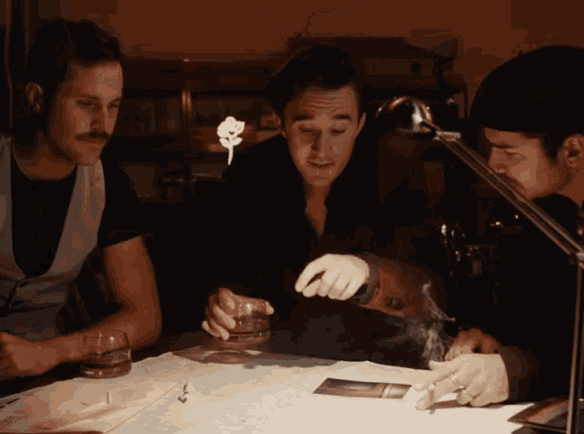three men are sitting at a table and one of them is smoking