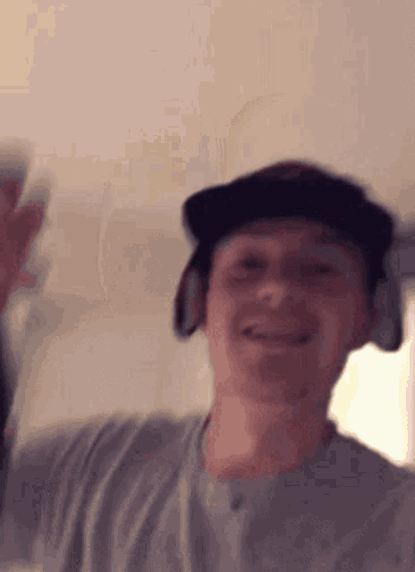 a man wearing headphones and a hat is smiling and waving his hand .